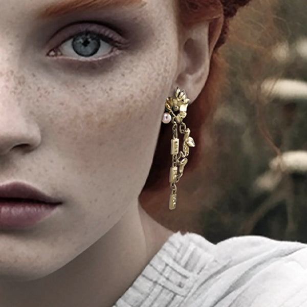 Gold floral earrings - Organic jewellery design in gold, with surreal leaves, chains, and a white pearl – on models ear - Livva