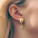 Heart drop earrings gold – A square design with tiny studs and a dangling heart worn by model – Livva Østerby.