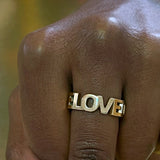 Bogstav ring med ordene LOVE LOVE LOVE sammensat som udskårne bogstaver i guld, vist i closeup på hånd - Livva