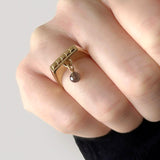 Gold square ring – Sleek square design with tiny studs and a smoky quartz dangle charm on hand close up – Livva Østerby.