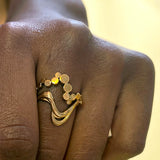 Wavy ring i guld - Unikt smykkedesign med snoet organiske bølger og flade bobler, vist i closeup på solbrun hånd - Livva